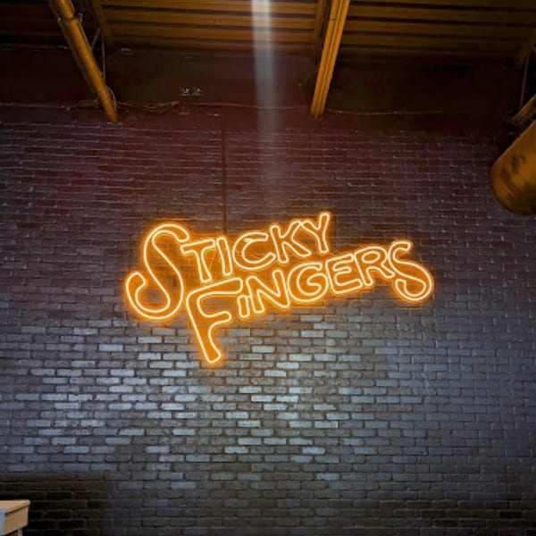 An orange neon sign spelling "Sticky Fingers" glows against a dark brick wall.
