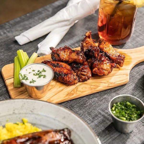 Sticky Fingers Rib House BBQ wings with celery, ranch, and a drink on a wooden board.
